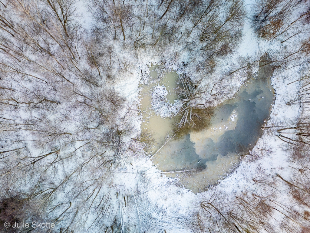 Drone image of snow covered forest with a heart shaped lake.